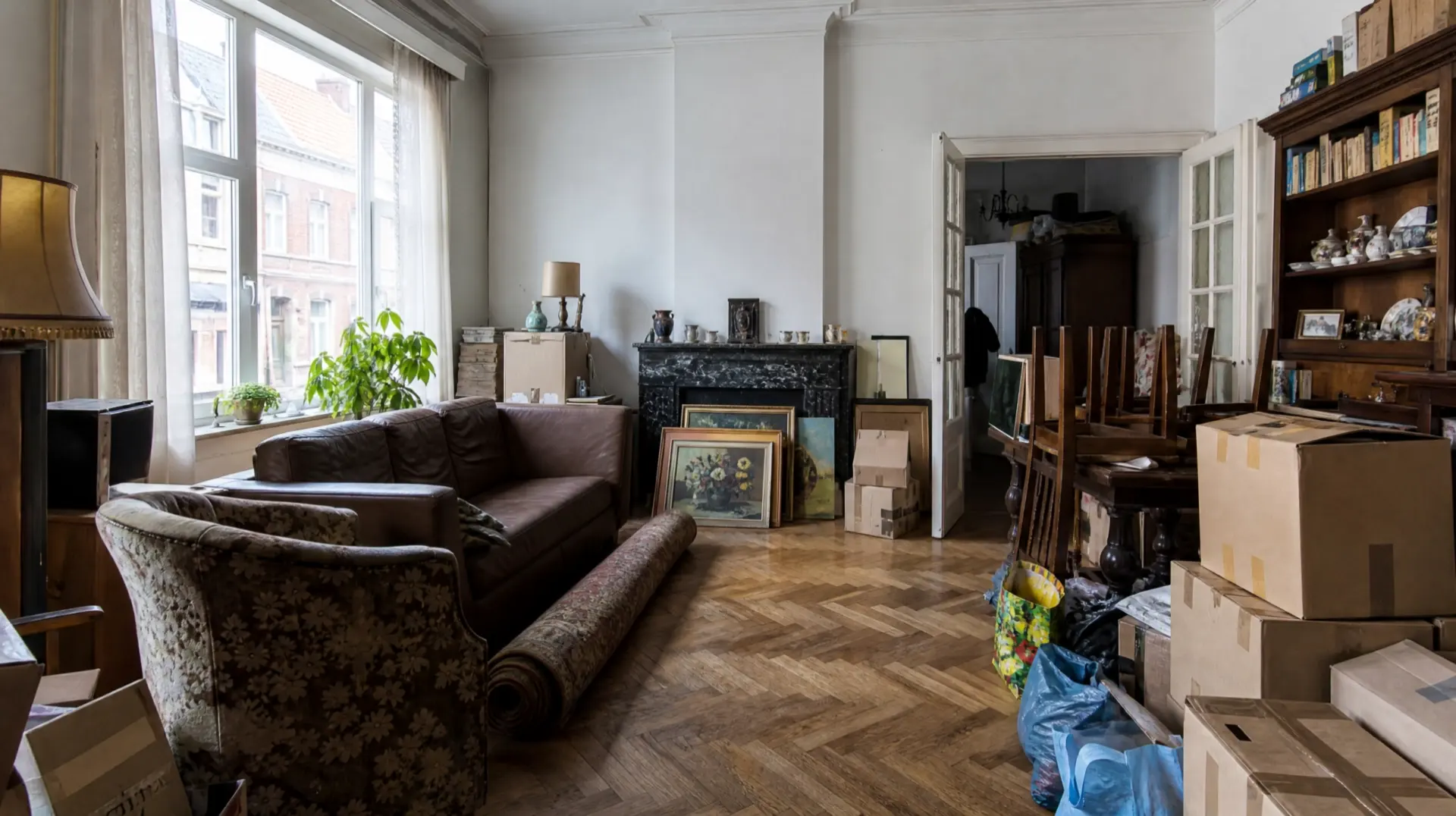 Full living room of a Belgian townhouse with sofas, boxes, paintings and an oak cabinet, just before a house clearance
