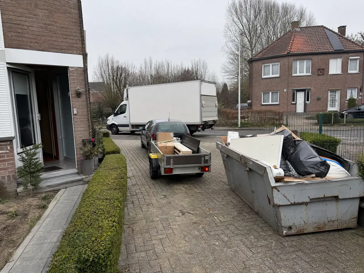 Skip and car trailer on a driveway of a house being cleared, with a white box truck on the street