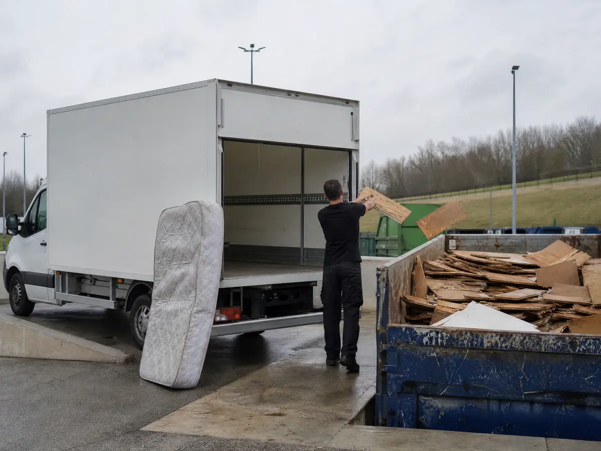 White box truck at the containers of a recycling park, a crew member throws wood into a container